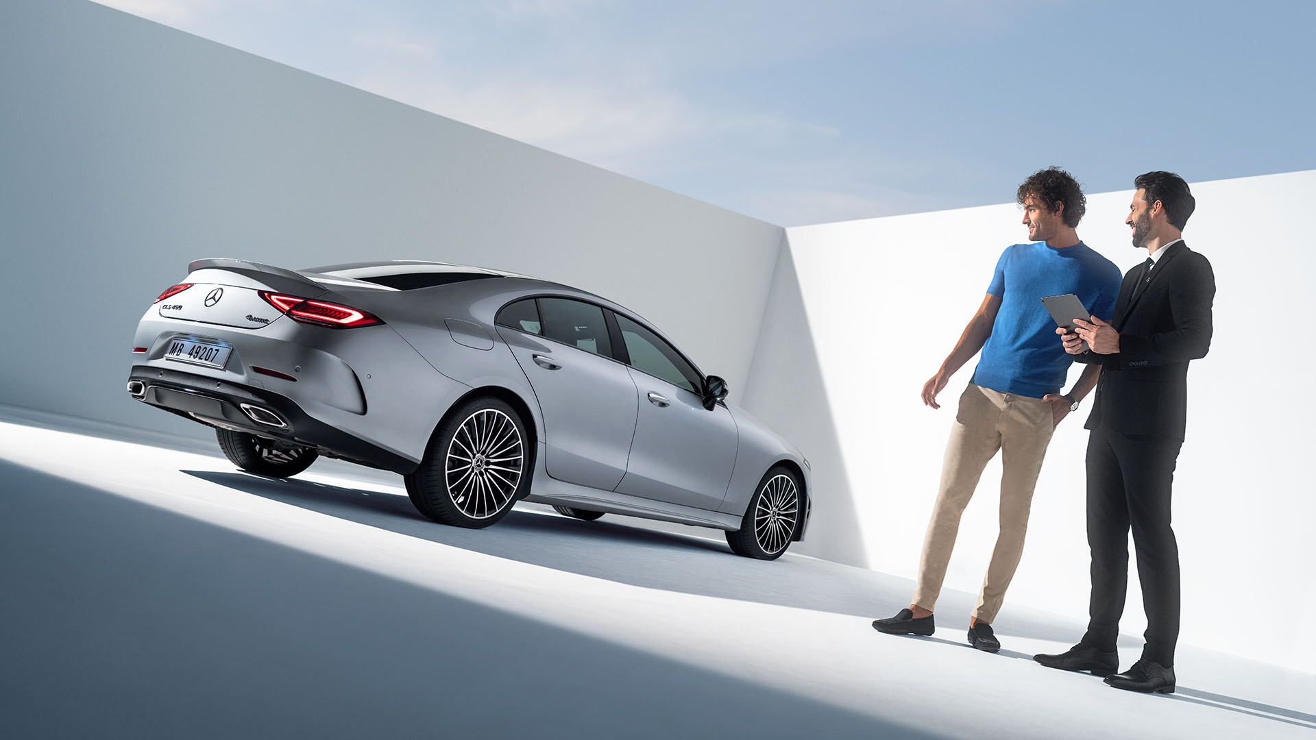 Ein Kunde und ein Verkäufer stehen vor einem sportlichen silbernen Mercedes-Benz CLS Coupé