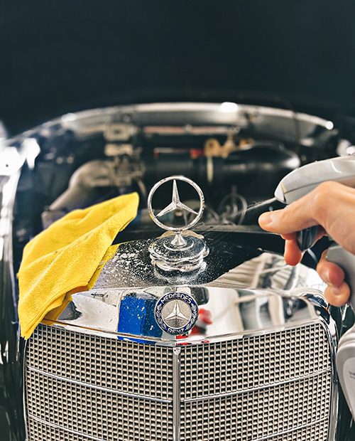 Ein Mercedes-Oldtimer wird mit einer Sprühflasche besprüht und geputzt